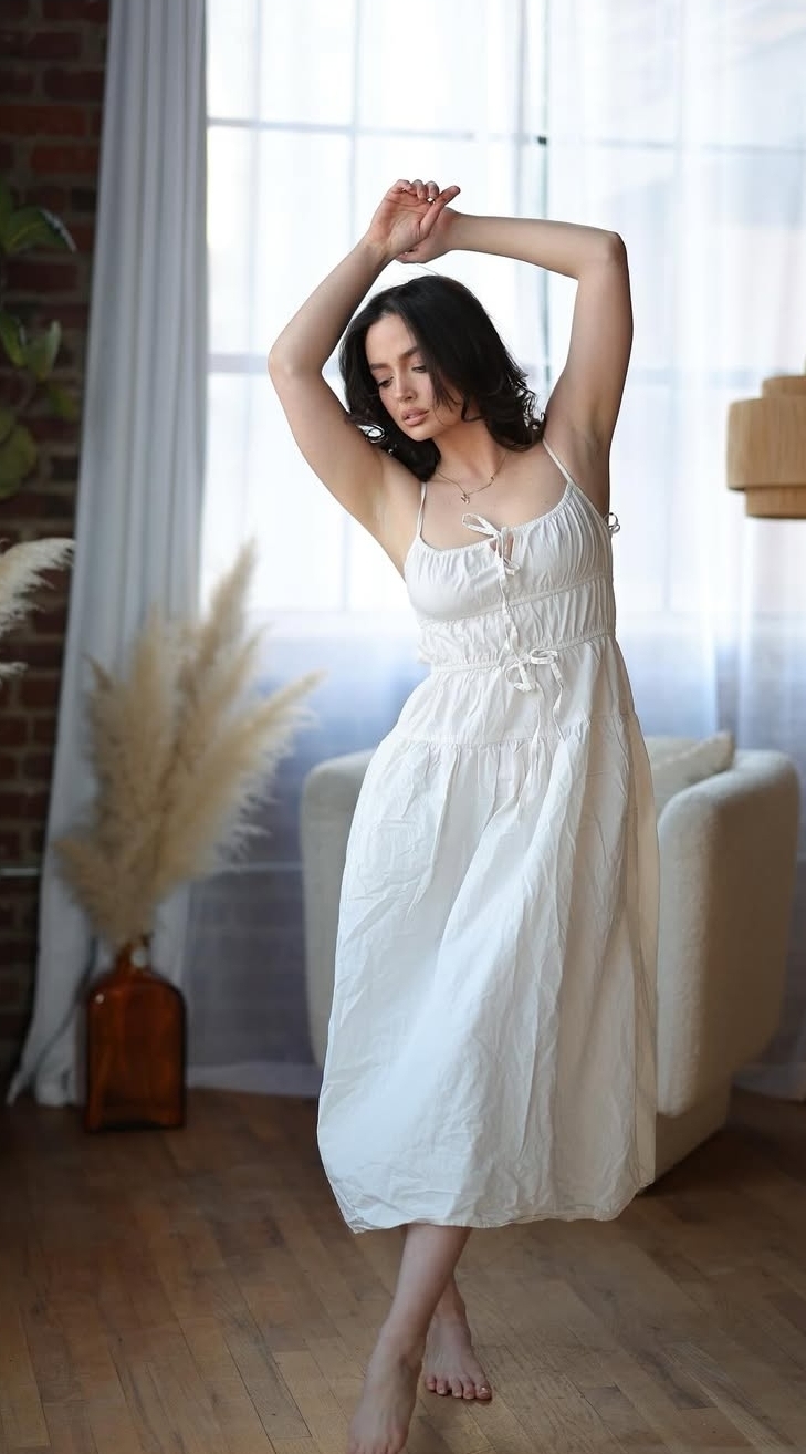 Mercy in a soft white dress posing by a bright window